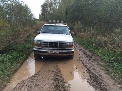 1993 Ford Bronco - White 1990s Ford Bronco navigates a muddy track surrounded by vegetation.