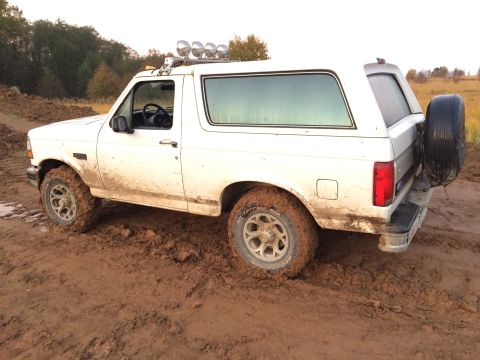 1993 Ford Bronco - This white Ford Bronco is stuck in the mud, with off-road lights on the roof and a spare tire mounted on the rear.