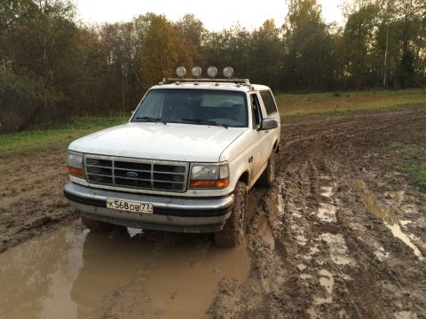 1993 Ford Bronco - This 1993 Ford Bronco navigates a muddy off-road track, equipped with auxiliary lights on its roof rack.