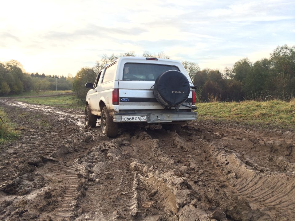 1993 Ford Bronco stuck in mud on a dirt road, rear view