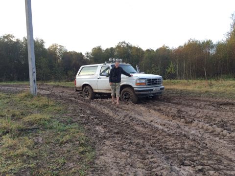 1993 Ford Bronco - A man stands by his white Ford Bronco, which is stuck in a muddy, off-road track.