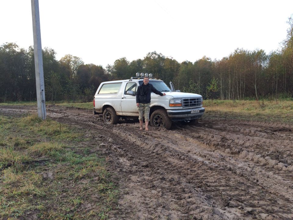 Guy next to white Ford Bronco stuck in mud, off-road lights on roof