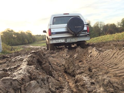 1993 Ford Bronco - A white Ford Bronco navigates a muddy track, its rear end visible as it struggles for traction.