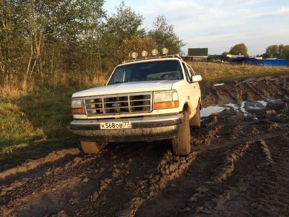 White 1993 Ford Bronco stuck in mud with roof lights