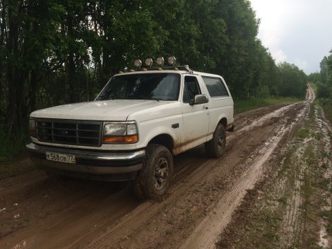 1993 Ford Bronco - This white Ford Bronco is driving on a muddy road through a wooded area.