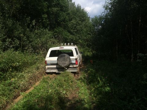 1993 Ford Bronco - A white Ford Bronco navigates a muddy trail surrounded by dense foliage.