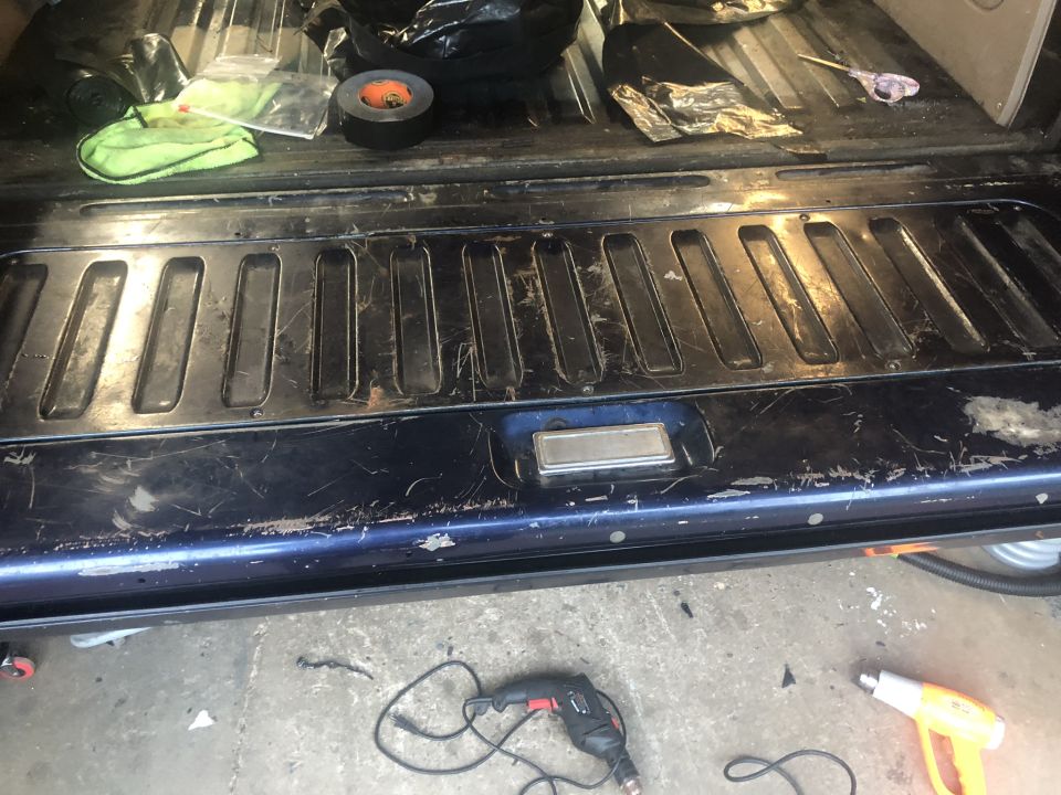 Back of a dark blue vehicle, showing the inside of the tailgate with some tools and cleaning supplies on top