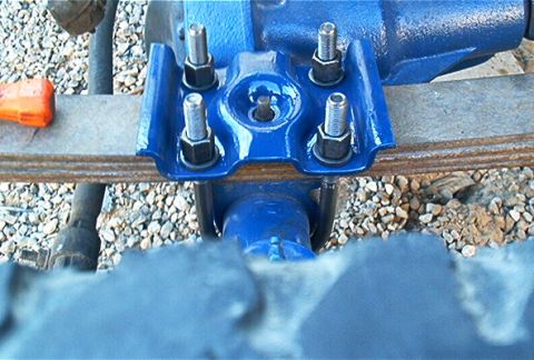 1986 Ford Bronco - Close-up of a freshly painted blue cast-iron component, likely a differential or steering/suspension bracket, secured with four large bolts…