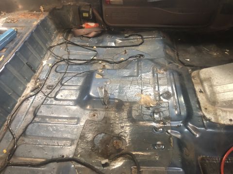 1995 Ford Bronco - The interior floor of a vehicle shows exposed metal, wiring, and signs of wear and tear.