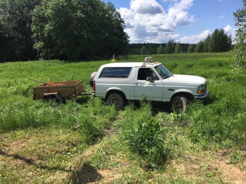 1993 Ford Bronco - A white Ford Bronco tows a wooden trailer through a field on a sunny day.