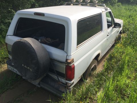 1993 Ford Bronco - White Ford Bronco with a spare tire on the rear door is stuck in the mud off-road.