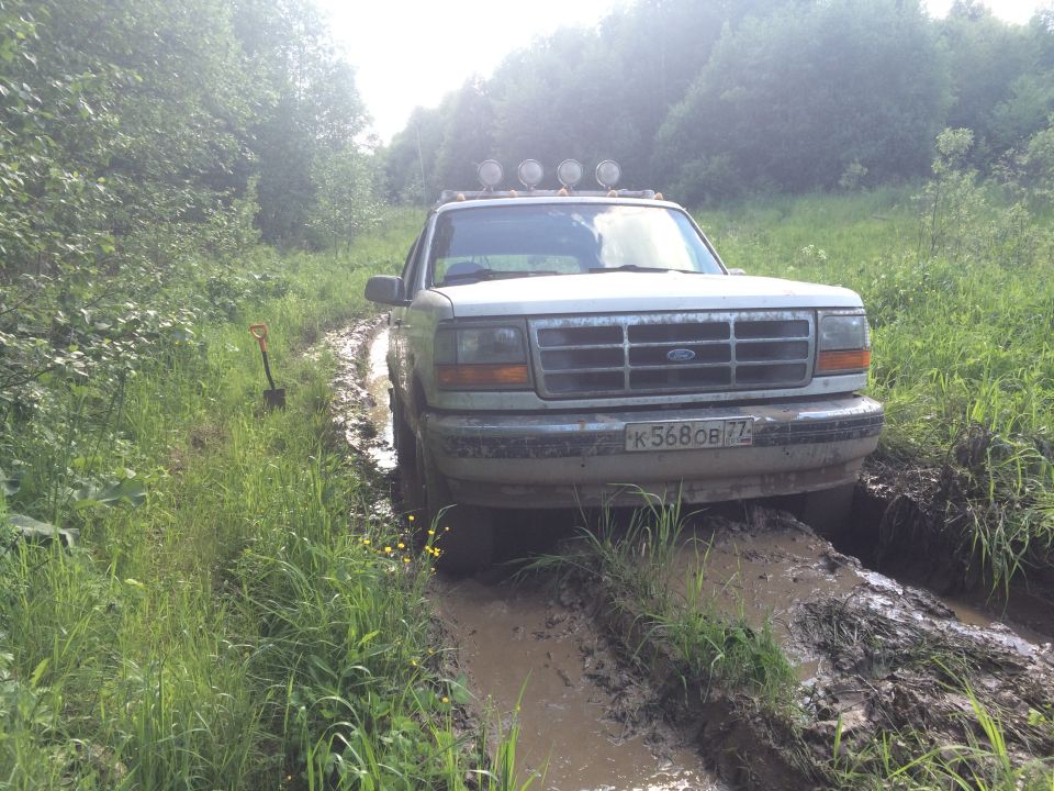 1993 Ford Bronco stuck in a muddy rut on a dirt road, with trees and grass on either side