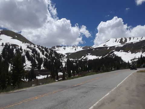 1999 Ford E250 - A scenic mountain road with snow-capped peaks and evergreen trees under a partly cloudy sky.