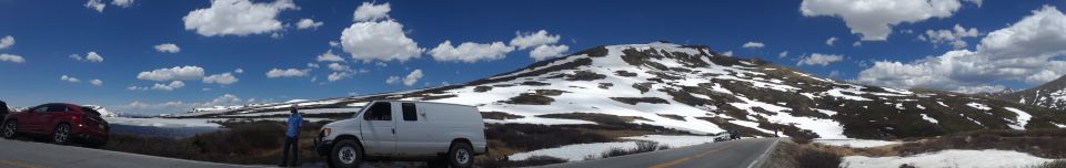White van and red car parked on a roadside with a snow-covered mountain under a blue sky with clouds