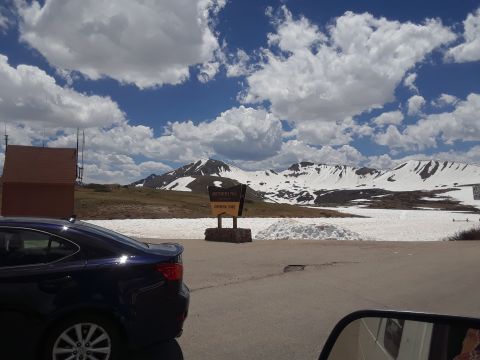 1999 Ford E250 - A dark blue sedan is parked near a sign with mountainous, snow-covered scenery behind it.