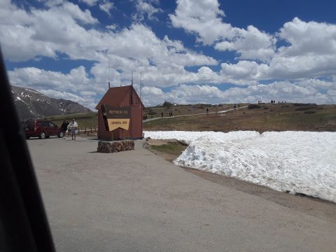 1999 Ford E250 - Independence Pass Continental Divide sign and building with snow piles, a red SUV is parked nearby.