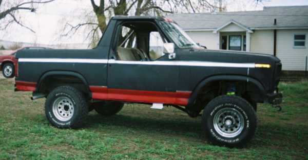Side profile of a black and red lifted Ford Bronco on chrome wheels on grass