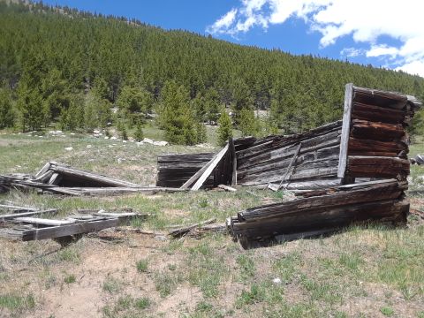 1999 Ford E250 - Abandoned wooden structure in a mountainous, forested area under a blue sky with clouds.
