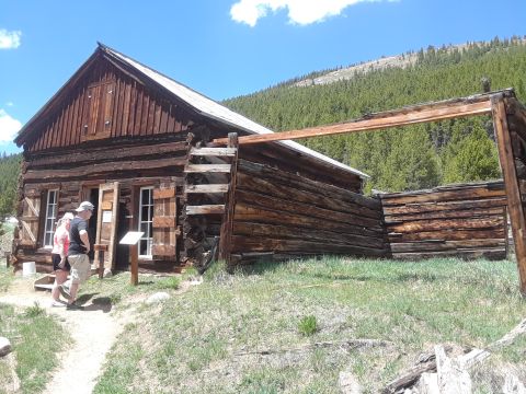 1999 Ford E250 - A rustic log cabin sits in a grassy area with a wooded mountainside in the background.