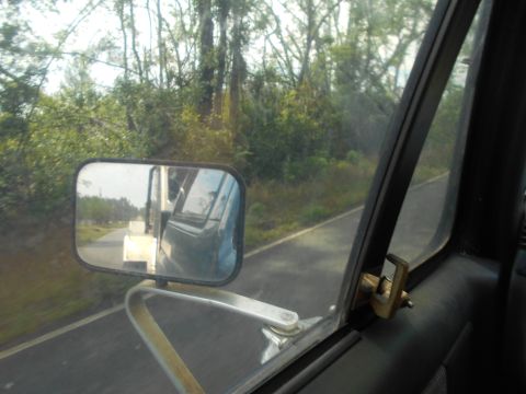 1992 Ford Bronco - Driving down a road, with trees and foliage visible outside the window and another vehicle in the side mirror.