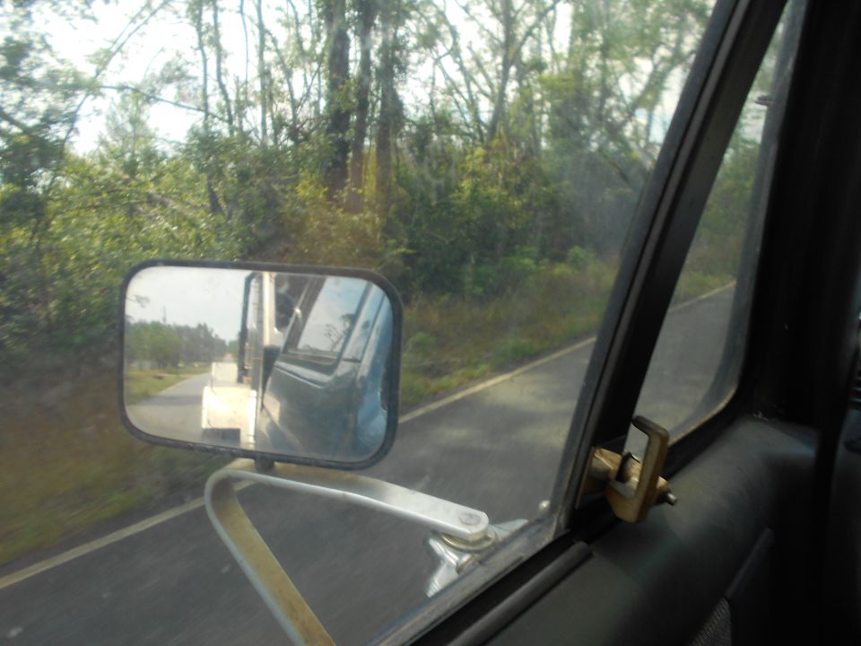 View from inside a vehicle, looking out the passenger side window and in the side mirror. Another vehicle is visible in the mirror