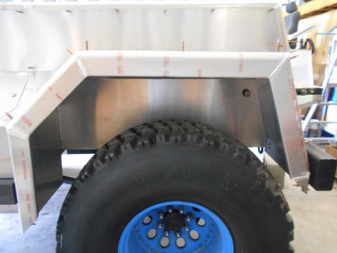 1992 Ford Bronco - Close-up view of the rear wheel well and tire on a vehicle with custom aluminum paneling and a bright blue wheel.