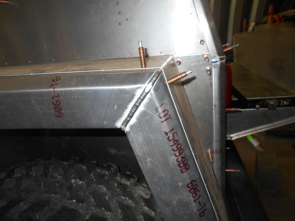 Close-up of a welded aluminum frame section with rivets and a tire visible