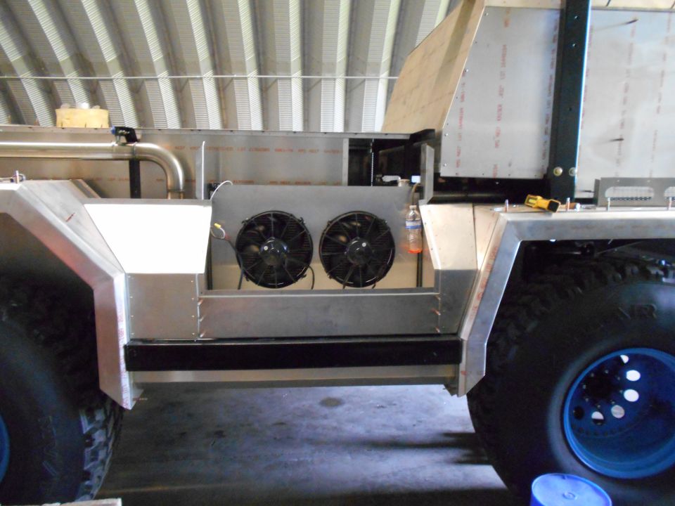 Side view of a custom vehicle's unfinished body with exposed frame, dual fans, and large tires