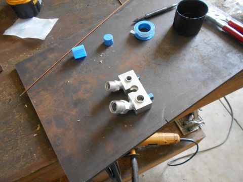 1992 Ford Bronco - A metal manifold with threaded fittings and blue caps sits on a workbench next to various tools and supplies.