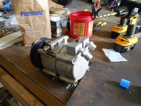 1992 Ford Bronco - An air conditioning compressor sits on a workbench next to a Fastenal bag and power tools.