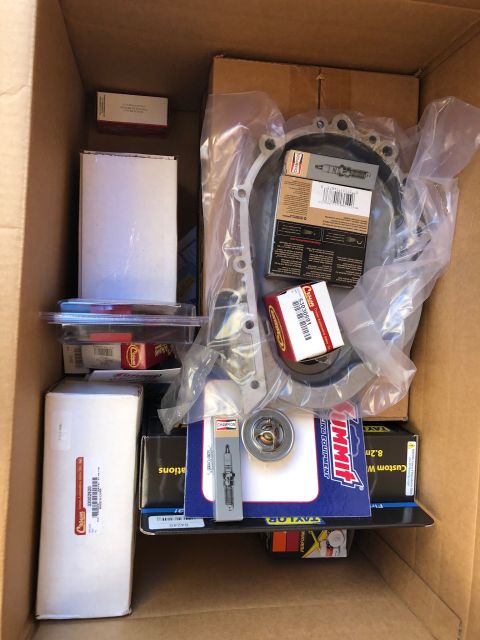 1992 Jeep Wrangler - Open cardboard box packed with new automotive parts including a gasket, thermostat, spark plugs and boxed components.