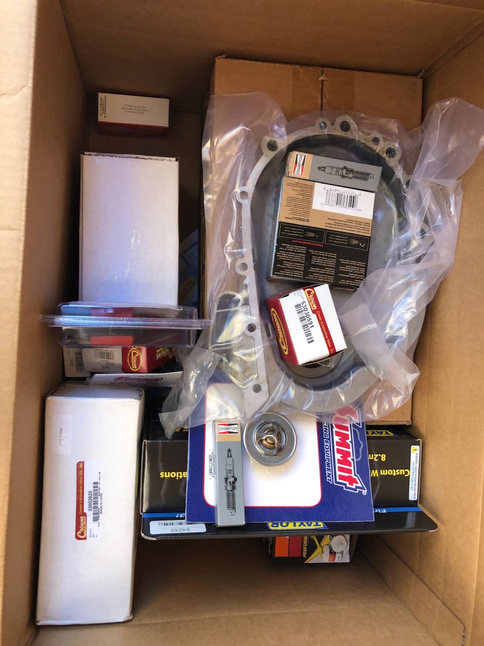 Cardboard box full of auto parts: gasket, thermostat, spark plugs and filters