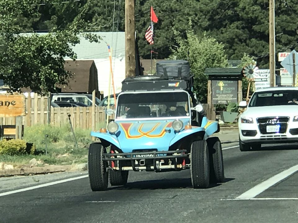 Blue dune buggy with yellow and red stripes, roof rack, and American flag driving on a road