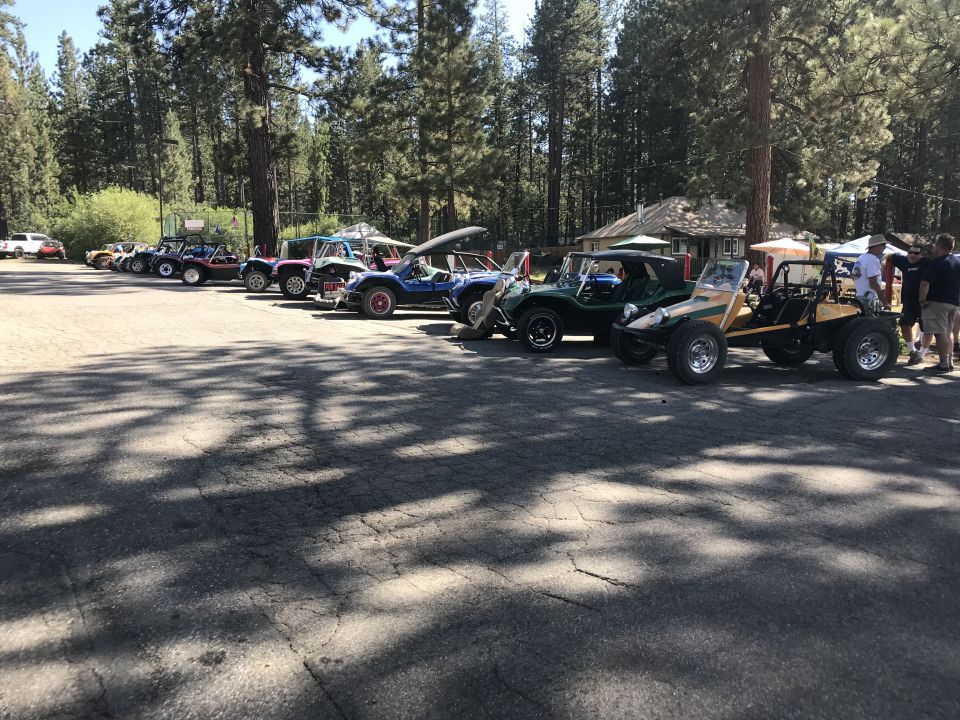 Several dune buggies parked in a lot with trees and a building in the background