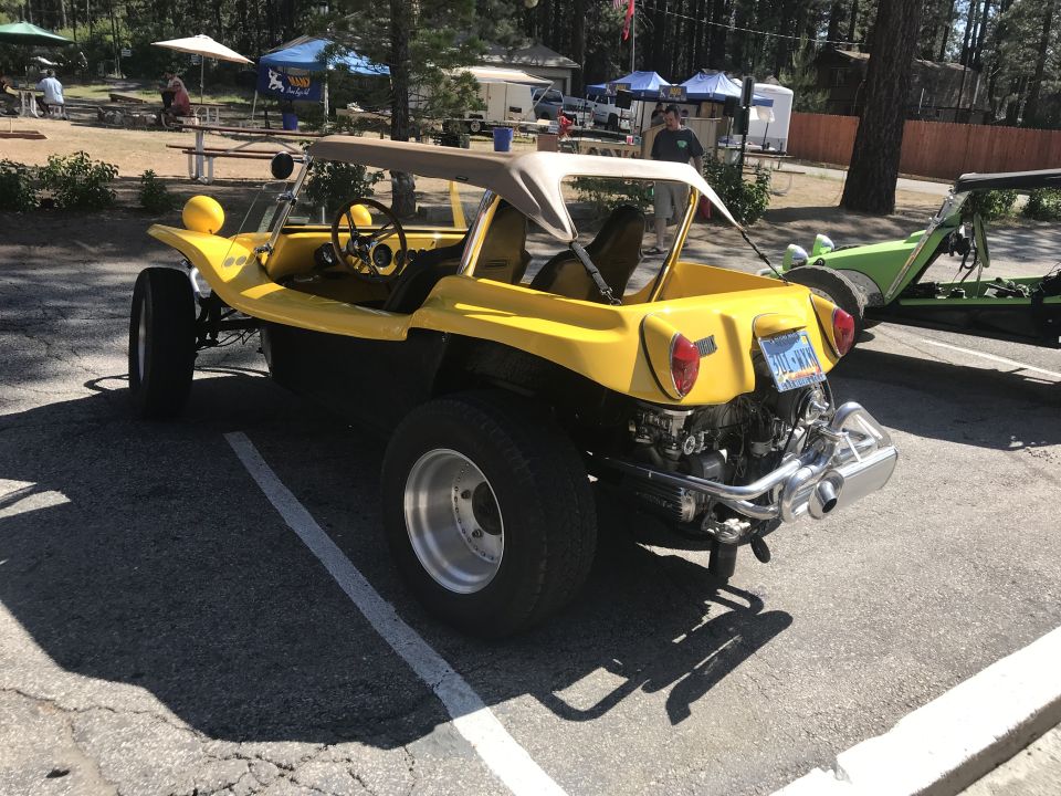 Yellow dune buggy with tan top, exposed engine, and custom exhaust. Another green buggy is visible behind it