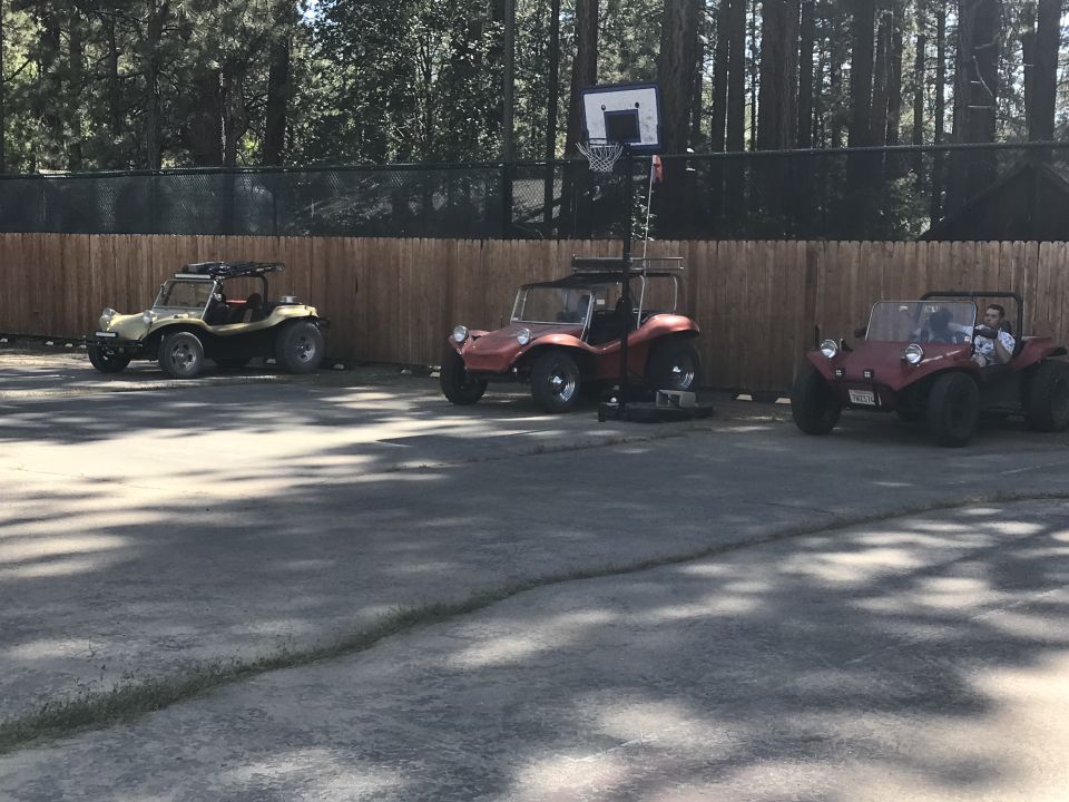 Three dune buggies parked in front of a wooden fence with a basketball hoop