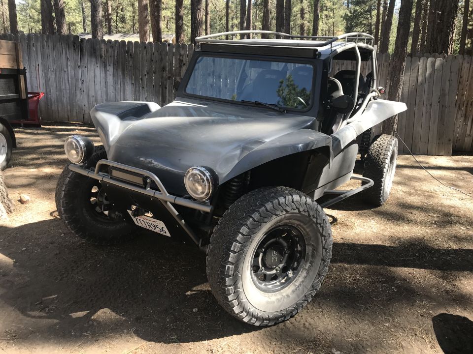 Gray dune buggy with off-road tires and a roll cage, parked outdoors