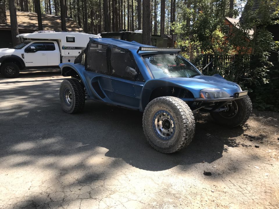 Blue custom buggy with large tires parked near a white pickup truck with a camper shell