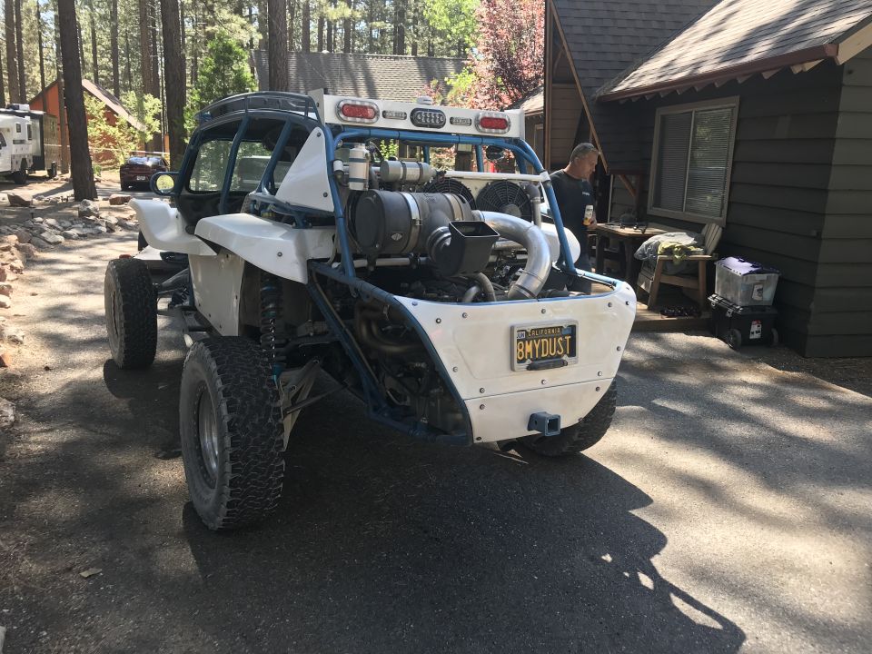 Rear view of a custom white dune buggy with a blue roll cage and exposed engine. California license plate reads 8MYDUST