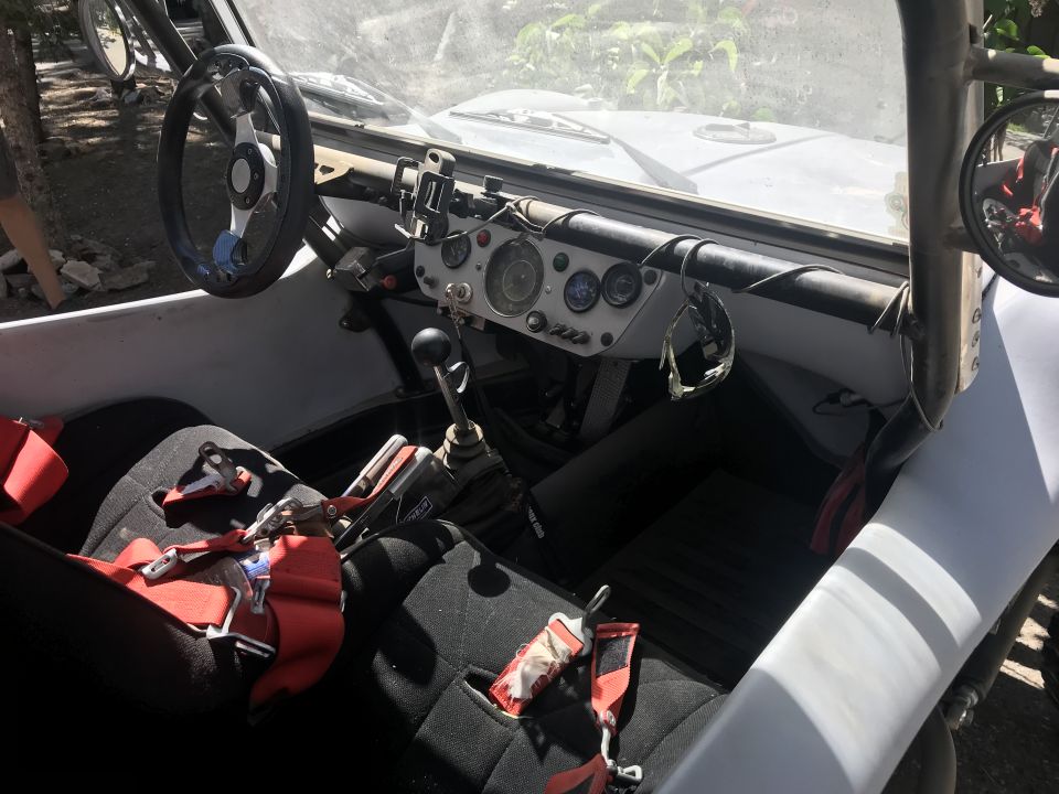 Interior of a dune buggy showing steering wheel, dashboard, seats, and gear shifter.