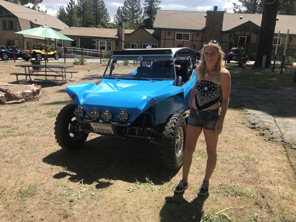 Woman standing next to a blue dune buggy with off-road tires and PIAA headlights.