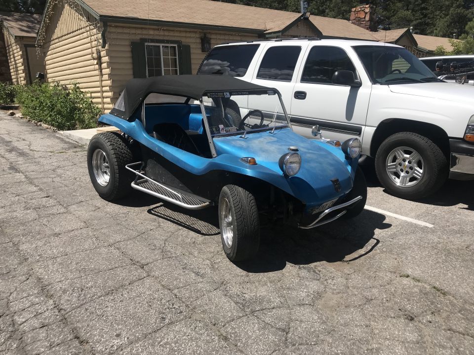Blue dune buggy parked next to a white SUV in front of a log cabin.