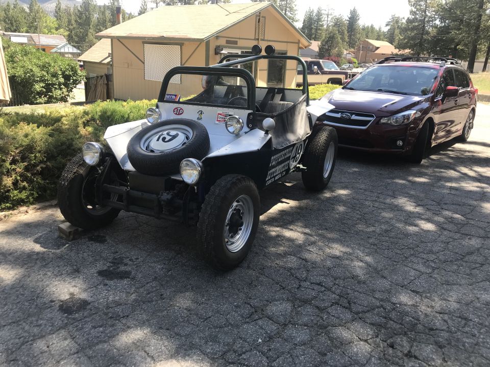 Silver and black dune buggy parked next to a red Subaru SUV.
