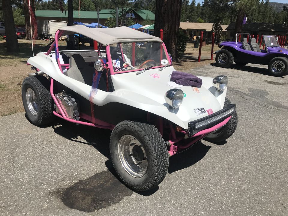 White custom dune buggy with pink roll cage and accents, parked on asphalt.