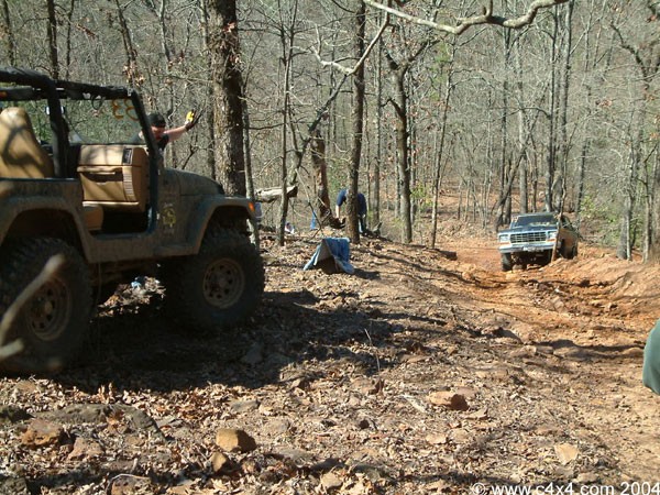 Brown Jeep and pickup truck on a muddy forest trail