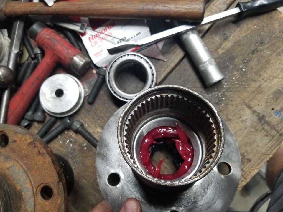 Wheel bearing assembly with red grease being applied, surrounded by tools like hammers and sockets