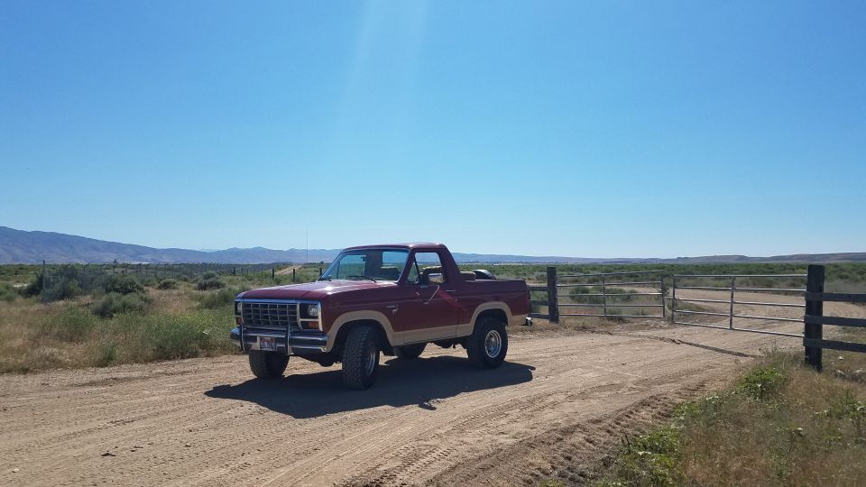 Maroon and tan 1980s Ford Bronco parked on a dirt road.