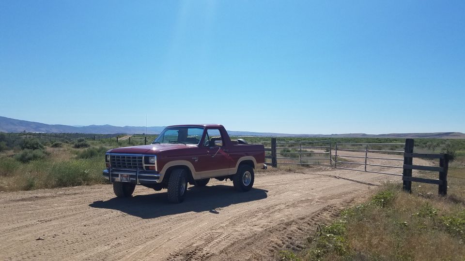 Maroon and tan 1985 Ford Bronco parked on a dirt road next to a gate.