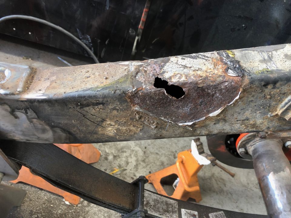 Close-up of rusted vehicle frame with a hole, supported by jack stands.
