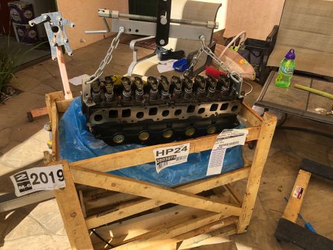 1992 Jeep Wrangler - Bare inline engine cylinder head with exposed valve springs mounted on a wooden stand outdoors, tagged HP24.